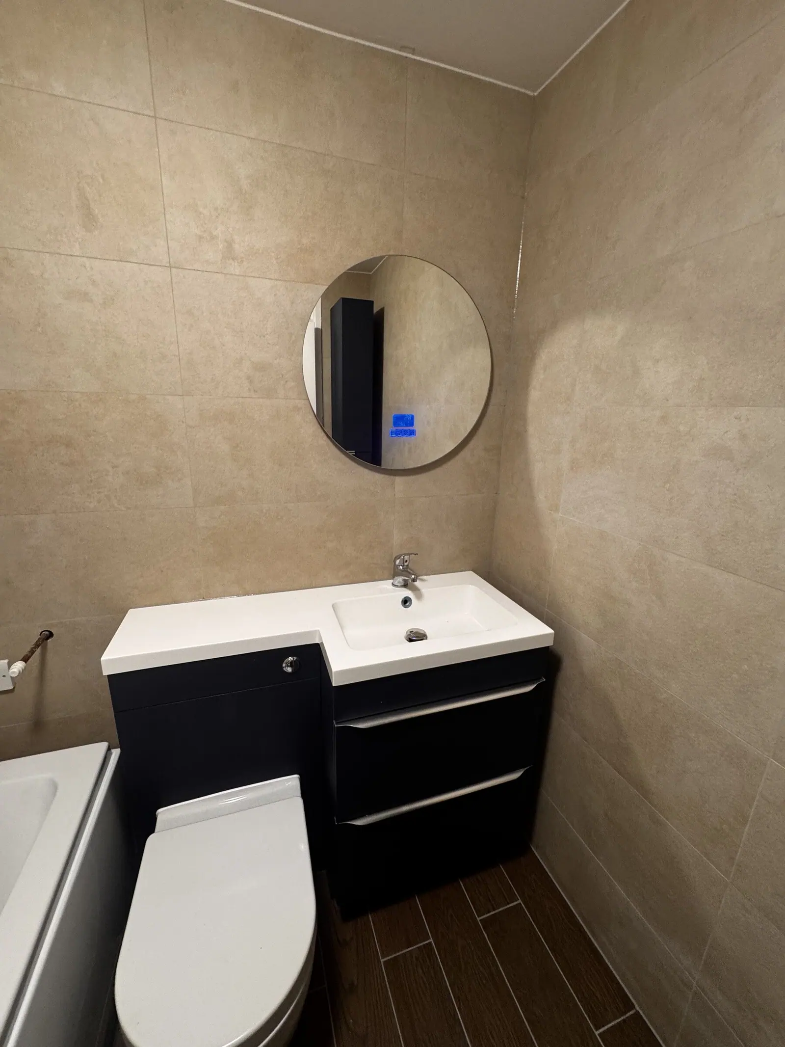Beige tiled bathroom with a navy wall-hung vanity, white basin and round mirror, fitted by Basingstoke Bathrooms