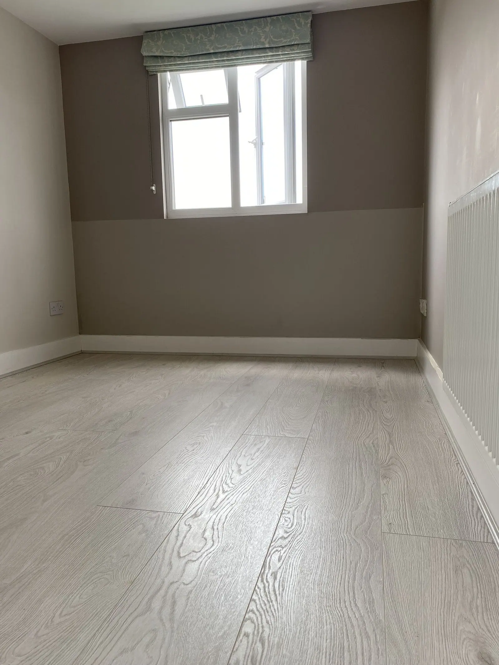 Freshly decorated bedroom with warm grey walls, white skirting and new oak-effect flooring, fitted by Basingstoke Bathrooms