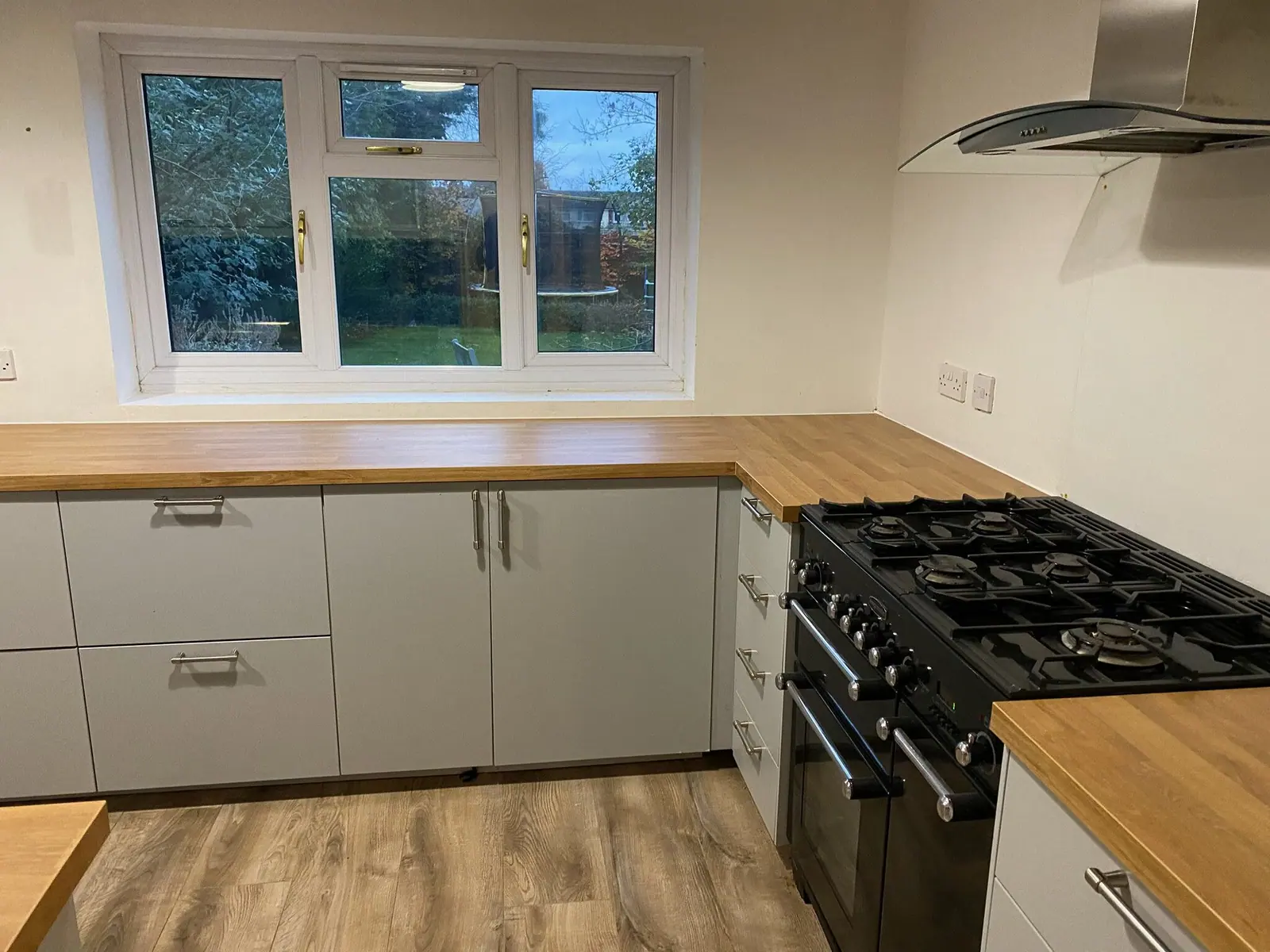 Kitchen with light grey units, solid oak worktops, black range cooker and chimney extractor, fitted by Basingstoke Bathrooms