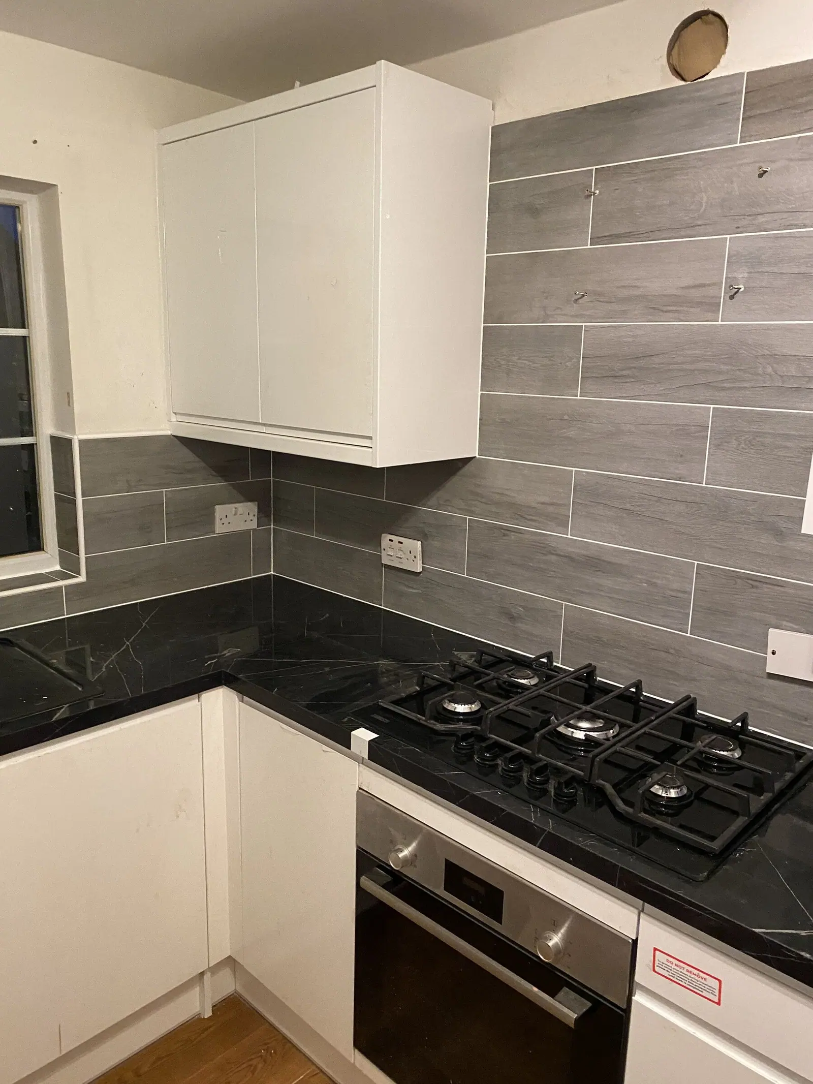 White gloss handleless kitchen with black marble-effect worktop, gas hob and grey wood-effect wall tiles, fitted by Basingstoke Bathrooms