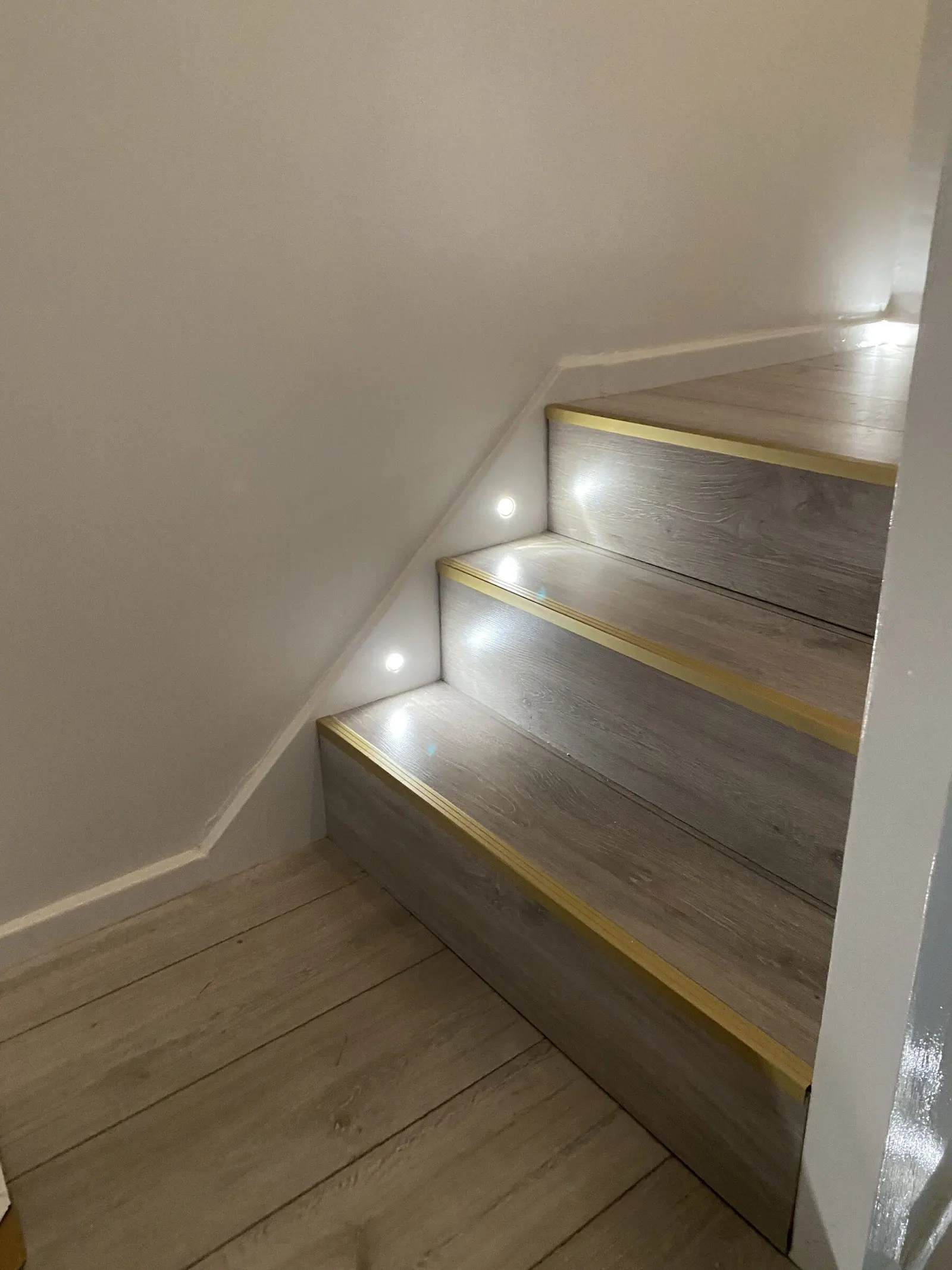 Renovated staircase with oak-effect treads, brass nosings and warm LED step lights, fitted by Basingstoke Bathrooms